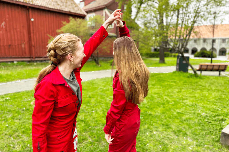 To russejenter som holder hender på en plen.