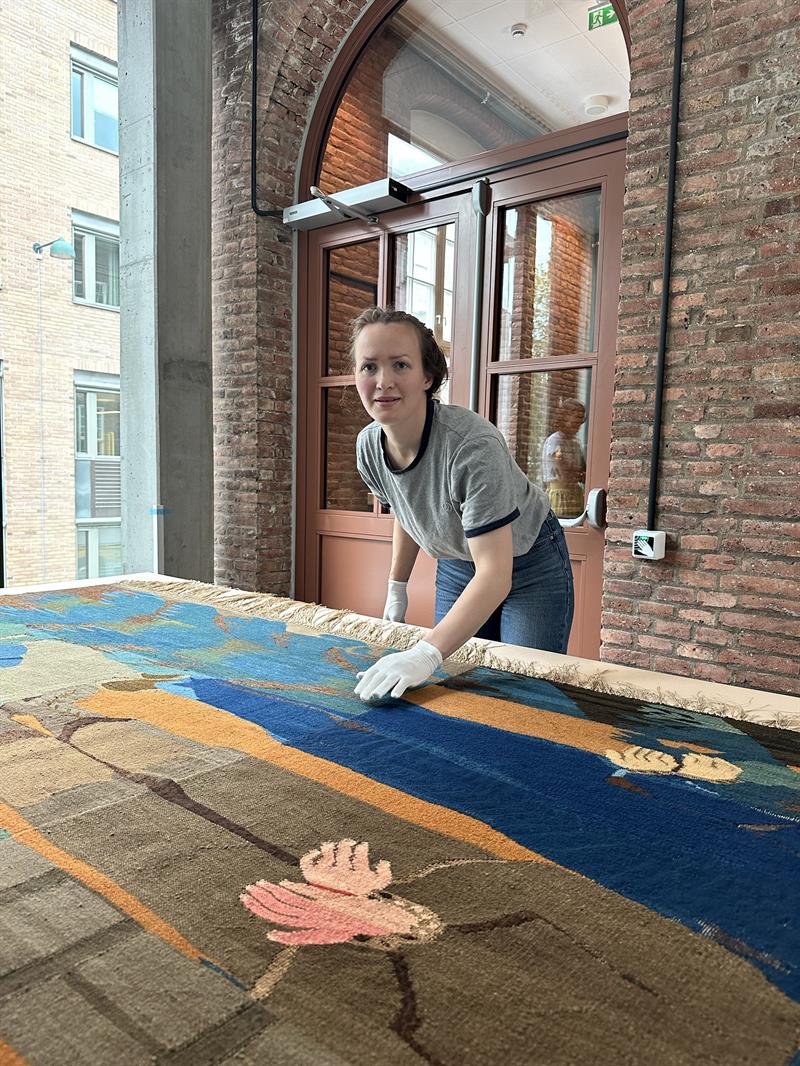 Bilde av kunstkonsulent Thea Wagner som styrker over billedveven Jeg risser ditt navn, Laurits Sand.