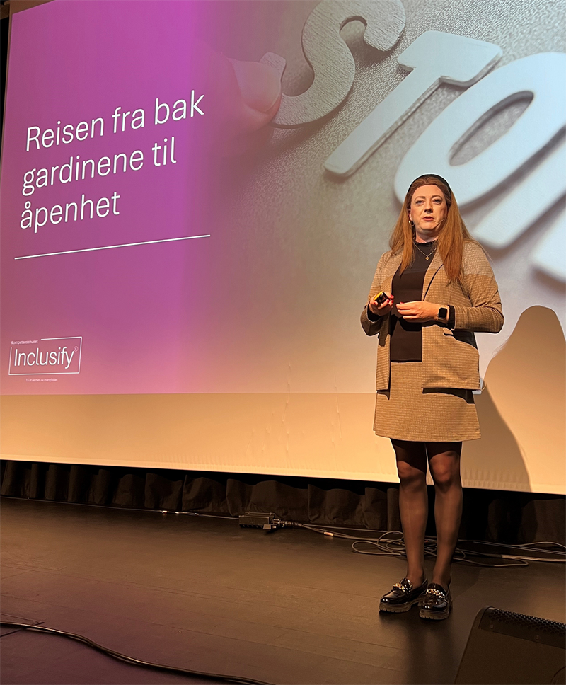 Torben (Cathrine) Dyhr Nielsen.png Transperson Torben (Cathrine) Dyhr-Nielsen, her som Cathrine på scenen. I bakgrunnen teksten "Reisen fra bak gardinene til åpenhet"