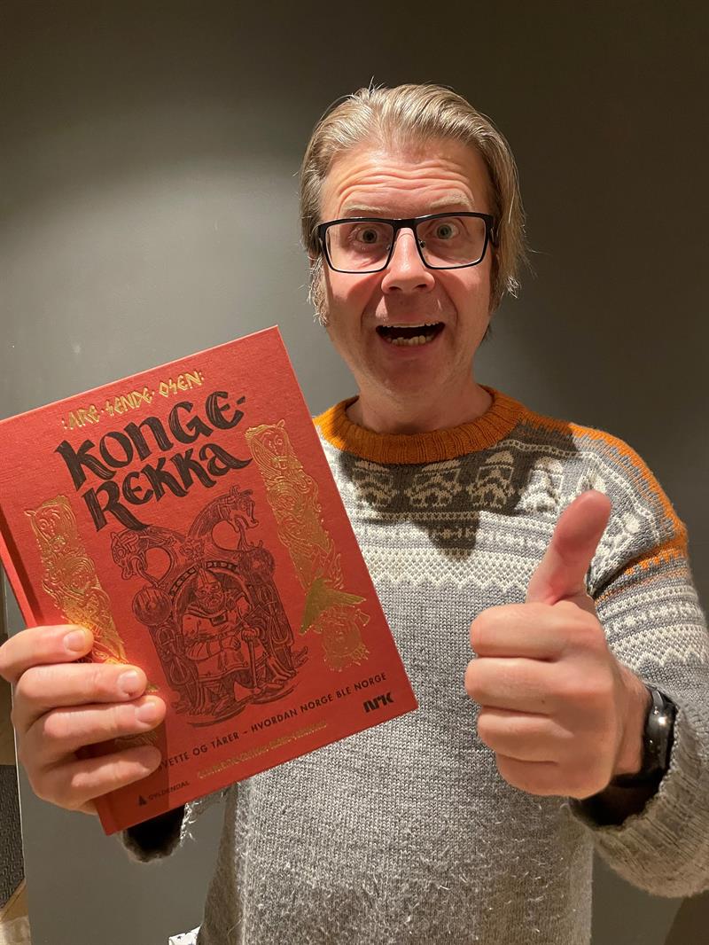 Are Sende Osen Portrettfoto av Are Sende Osen. Han holder boka Kongerekka i hånda og en tommel opp.