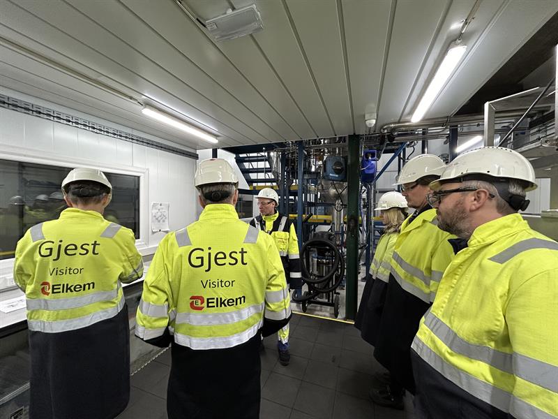 Omvisning2.jpeg Seks personer i gule arbeidsjakker står i et rom på en fabrikk. Industribedriften Elkem viser frem verdens foreløpige eneste gassatomiserer, som kan fremstille finkornet metallspon til bruk i 3D-printing av metalldeler. Foto: Syver Lie Rønningen