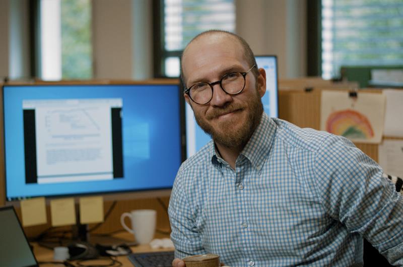 Mann på kontor. Foto Jon Skår en mann på et kontor står og holder en kaffekopp. Foto: Berre