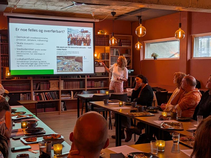 En kvinne holder en presentasjon. Lerret i bakgrunn og folk som ser på i forgrunn.