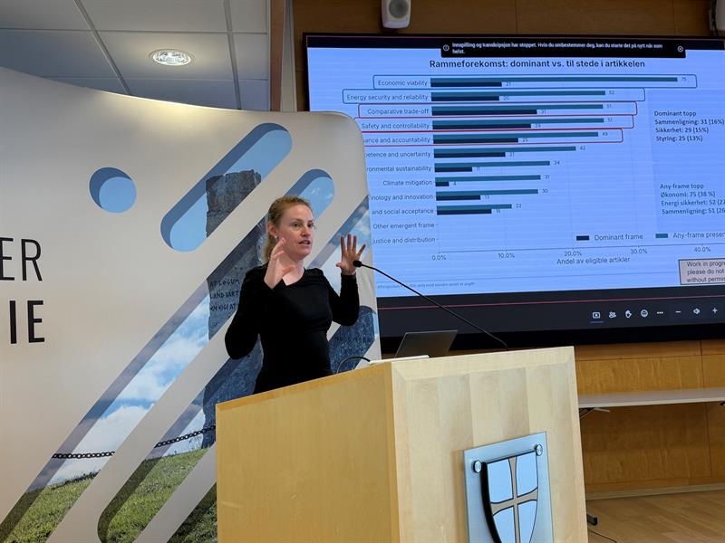 Silje Kristiansen (UiB) står og snakker fra en talestol. I bakgrunnen er hennes presentasjon.