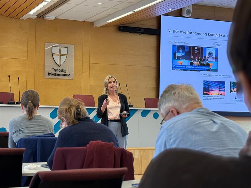 Audhild Kvam fra Tensio står og holder et innlegg. Foran henne ser vi bakhodet til tre personer.