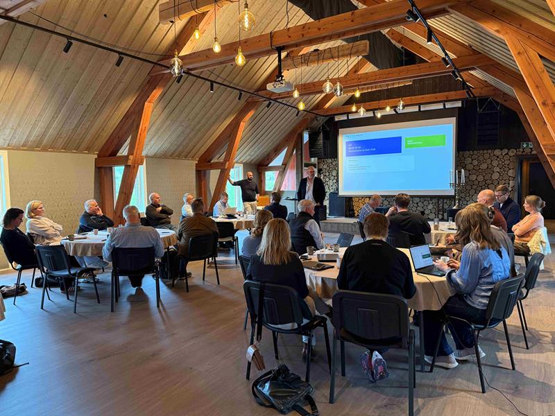 23 personer sitter i et konferanserom rundt fire rundbord. De ulike industri-hubene presenterte status, planer og utfordringer i utviklingen av egne områder. Samlinga var lagt til Hamna gård. Foto: Ida Valsø, Trøndelag fylkeskommune.
