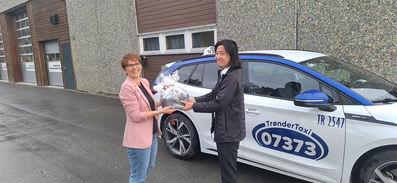 taxi-pilot-foto-rindal-kommune.jpg Ordfører Mildrid Kattem Aune deler ut blomster til Jo Kim Bolme Evjen, den første sjåføren i taxiprosjektet i Rindal kommune. Foto: Rindal kommune.